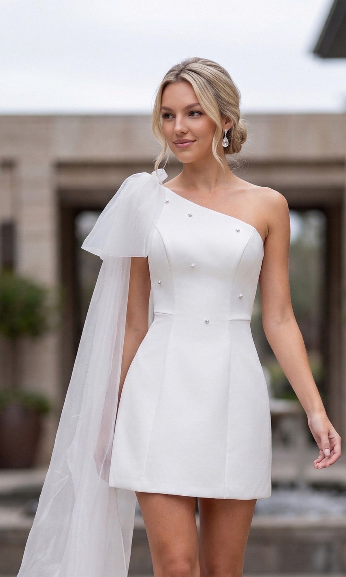 Woman wearing the Nox Anabel Y7003W White Mini Hoco Dress, featuring a short one-shoulder design with a sheer, flowing sleeve—ideal for rehearsal dinners or making a stylish statement at any special event.